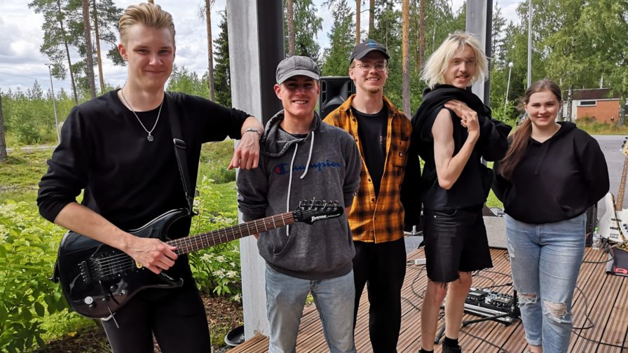 Viisi nuorta seisovat rivissä, joista yhdellä on kitara.