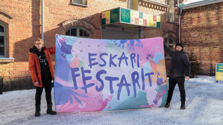 kaksi henkilöä kannattelee Eskarifestarit lakanaa Kalevan Navetan edessä