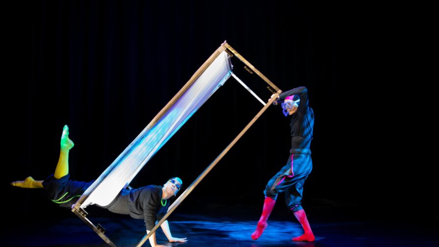 kaksi henkilöä taiteilee esiintymisasut yllään metallisen kehikon kanssa