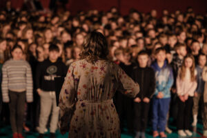 Koululaisia laulamassa isossa kuorossa. Etualalla kuoronjohtaja.